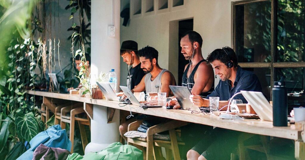 Group of digital nomads working on laptops in a tropical coworking space, surrounded by lush greenery and natural light in Bali